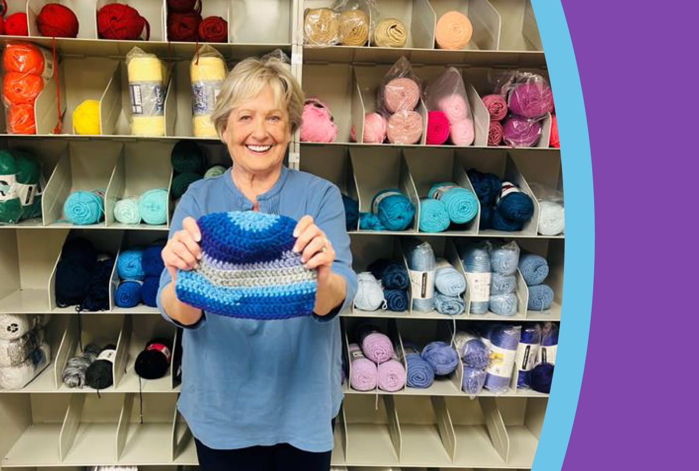 Forty Thousand Hand-Knit Happy Caps and Counting Kathy DeJoseph holding a knitted hat in front of wall of yarn
