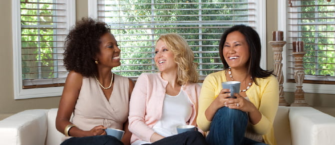 Three women chatting on the couch drinking coffee.