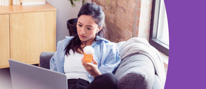 Person sitting with laptop, holding medication bottle