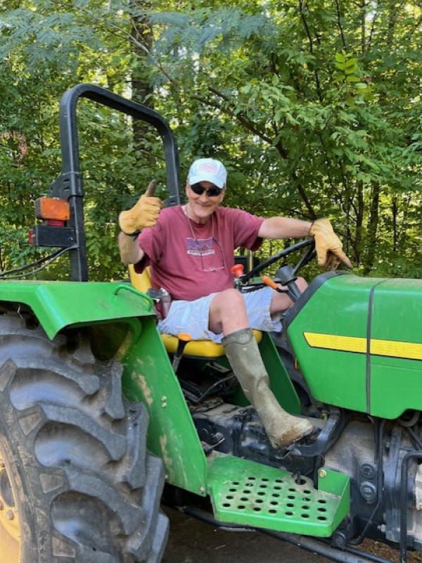 Three months after his deep brain stimulation (DBS) procedure at Wellstar, John grins and gives a thumbs up from the seat of his tractor as he gets ready to bushhog the family farm.